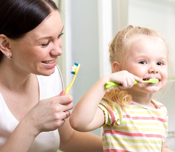 Mother helping her daughter brush her teeth