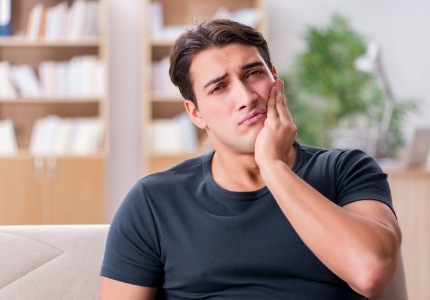 Man in need of emergency dentistry holding cheek in pain