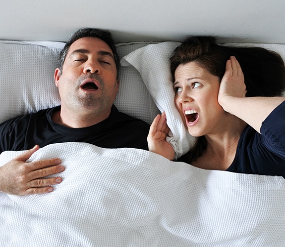 Frustrated woman next to snoring man in bed